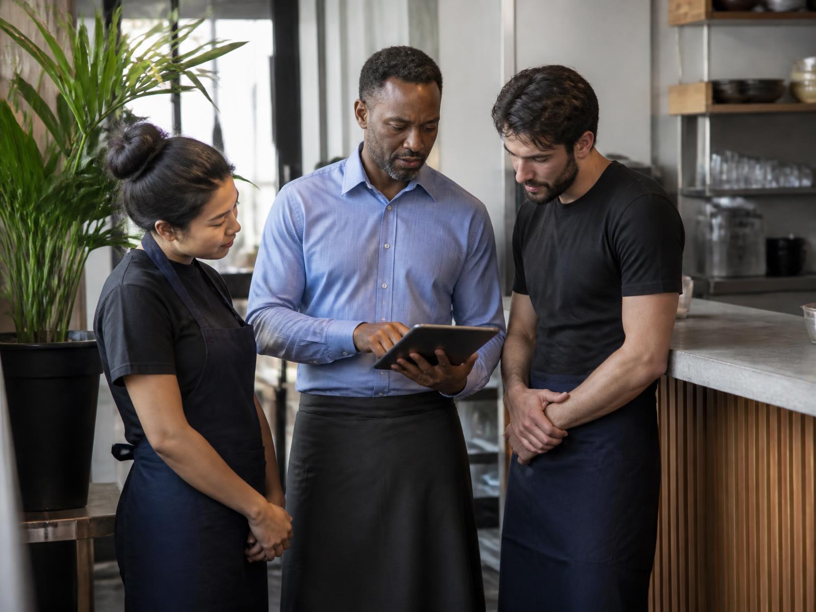 Restaurant manager reviewing the shift on a tablet with two team members in aprons near the service counter